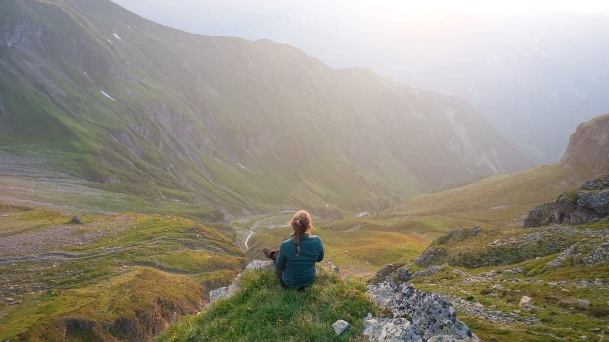 Woman sitting peacefully on a mountain cliff, looking out over a green valley