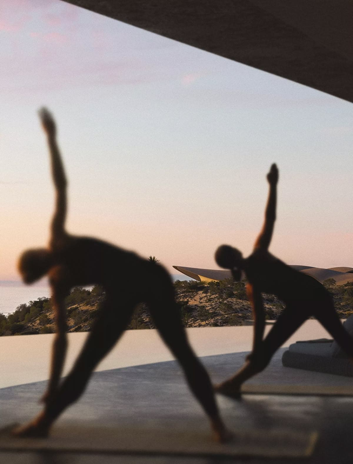 Two people silhouetted doing yoga at sunset on an outdoor terrace
